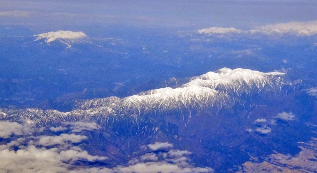 Vista aérea das cadeias montanhosas do Japão com picos nevados entre nuvens — barreiras naturais que isolaram populações caninas durante séculos